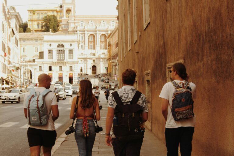 Four tourists with backpacks walking on a street in Rome, Italy, with historic architecture around.